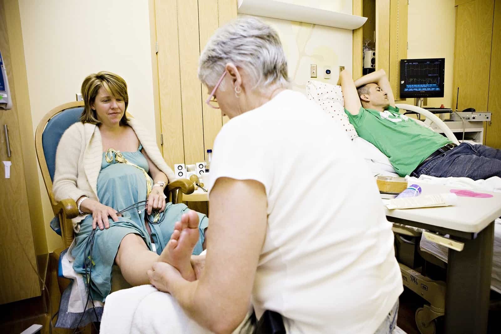 Pregnant woman enjoying a foot massage from doula while partner takes a break.