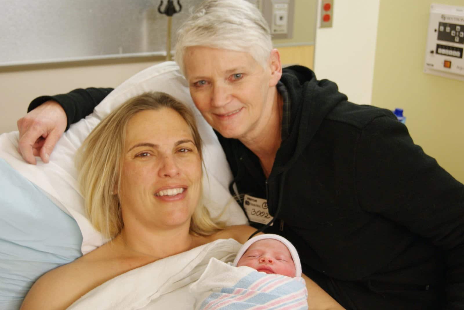 Happy new mother holding baby. Smiling for the camera with her doula.